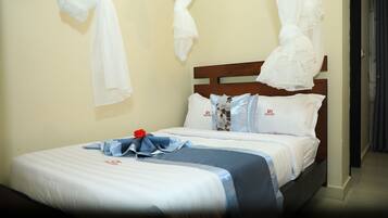 A neatly made bed with white and blue bedding, a wooden headboard, and a red rose on the bedspread.