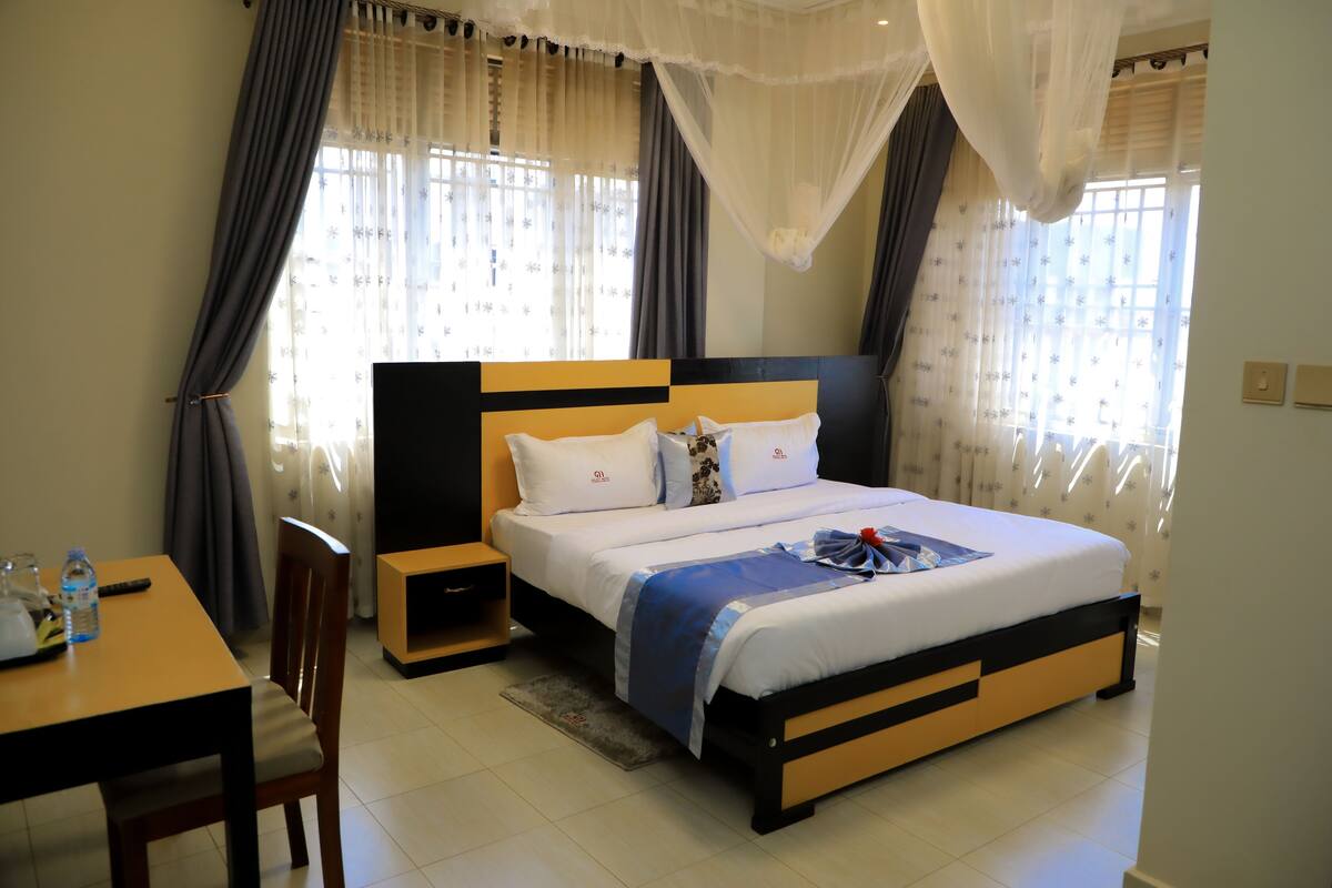 Un dormitorio con cama, mesitas de noche, una silla y cortinas.
