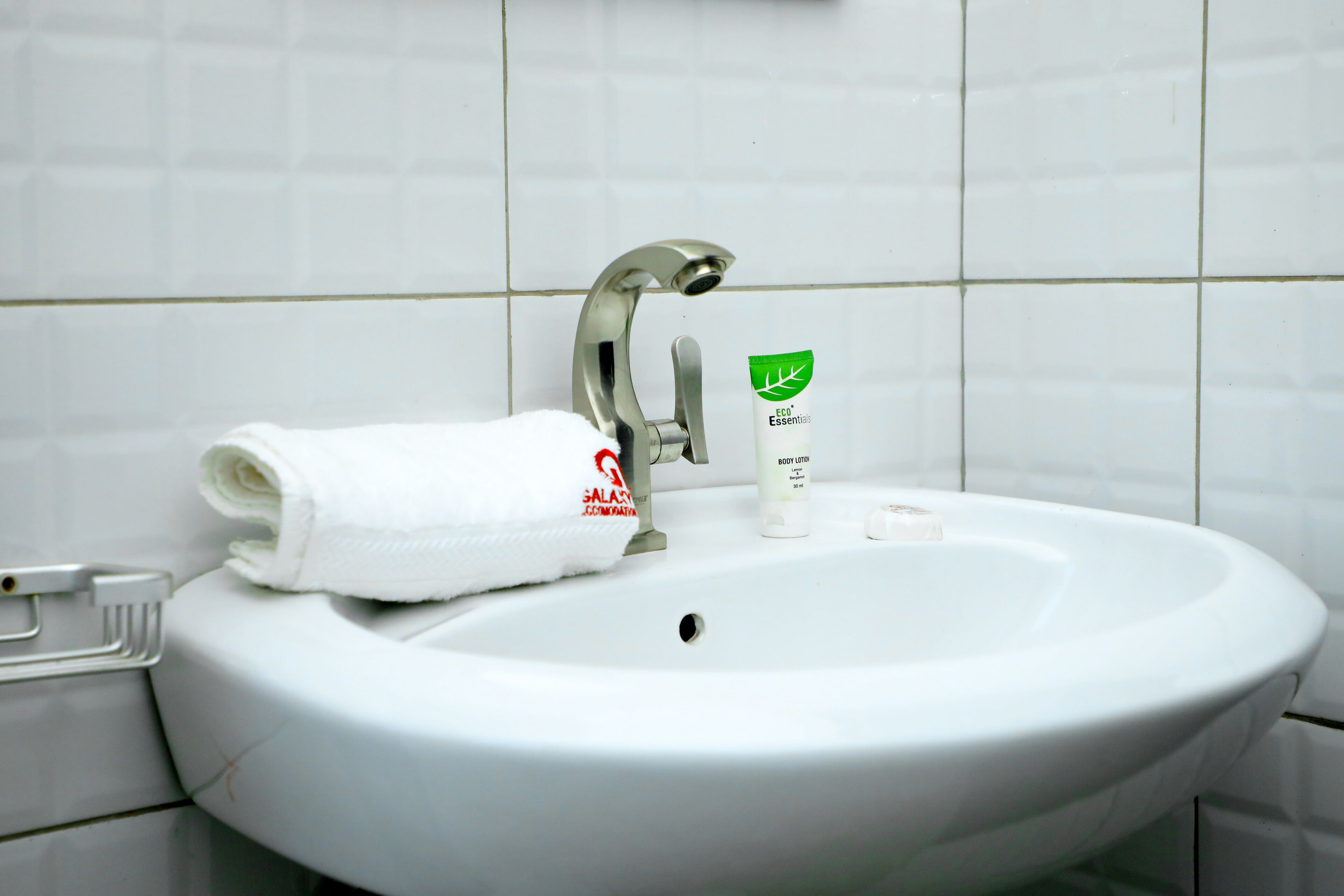 A white bathroom sink with a silver faucet, a white towel, and a body lotion tube.