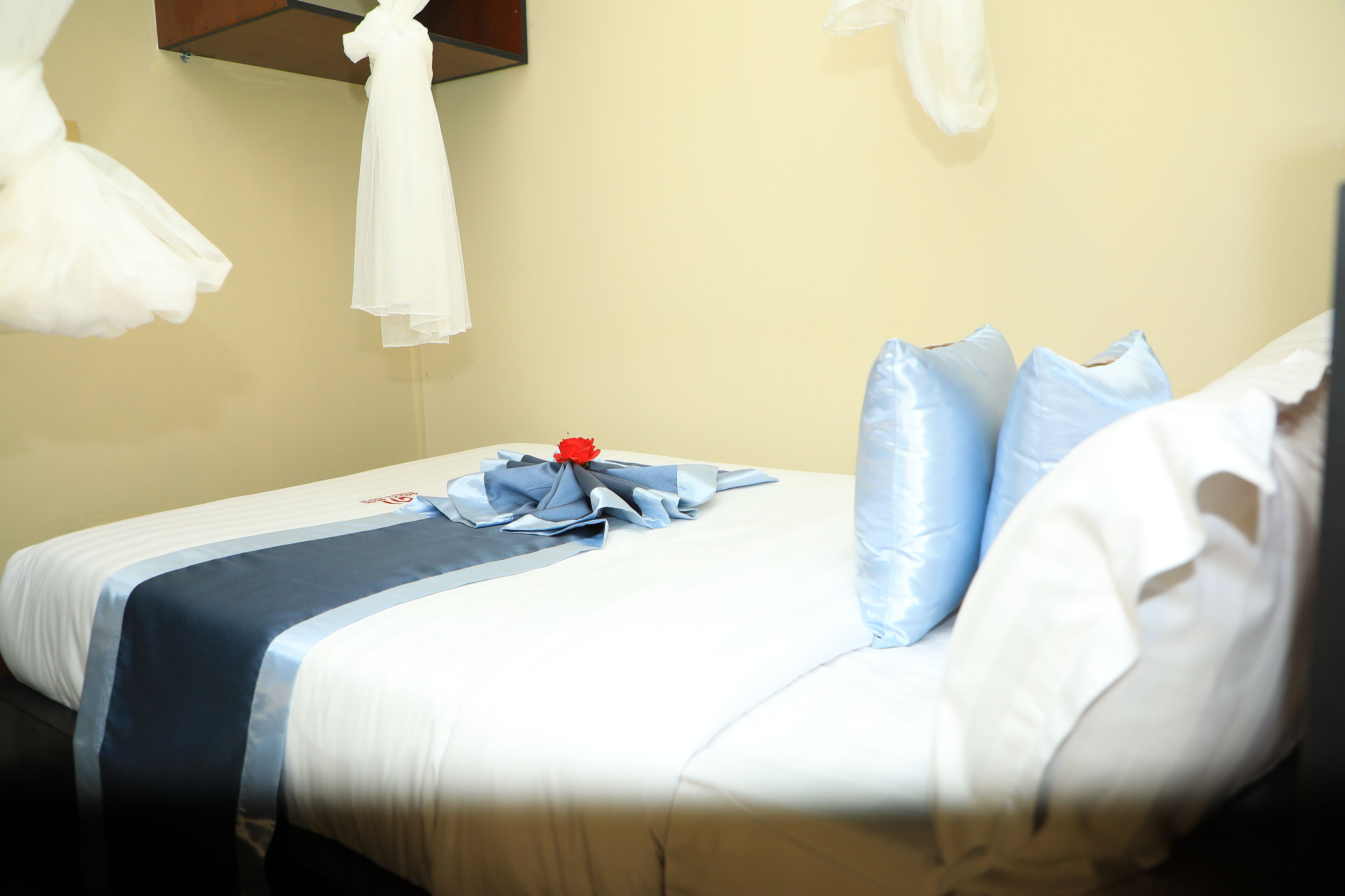 A neatly made bed with a blue and white bedspread, white pillows, and a red flower decoration.
