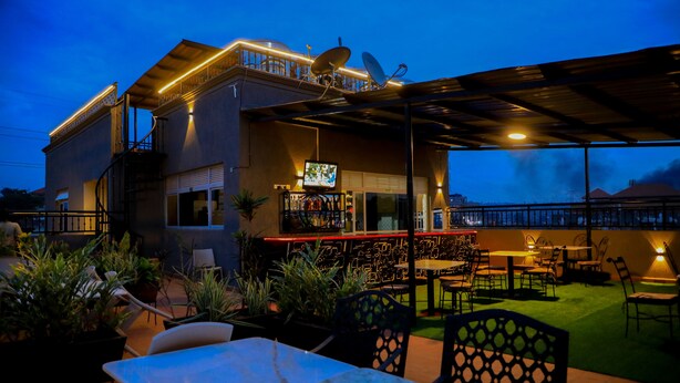 Un espace extérieur aménagé en terrasse, avec un bar, des sièges et une vue sur le paysage urbain au crépuscule.