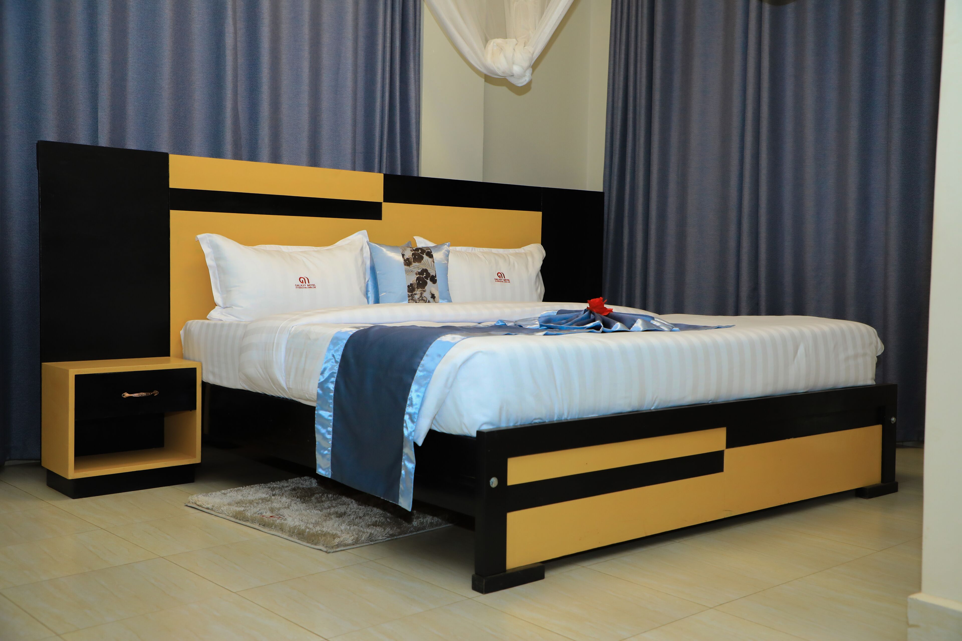 Een moderne hotelkamer met een bed, nachtkastje en een klein houten ladekast.