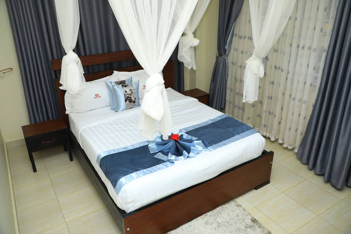 Una cama bien hecha con colcha azul y blanca, cabecera de madera y dosel.