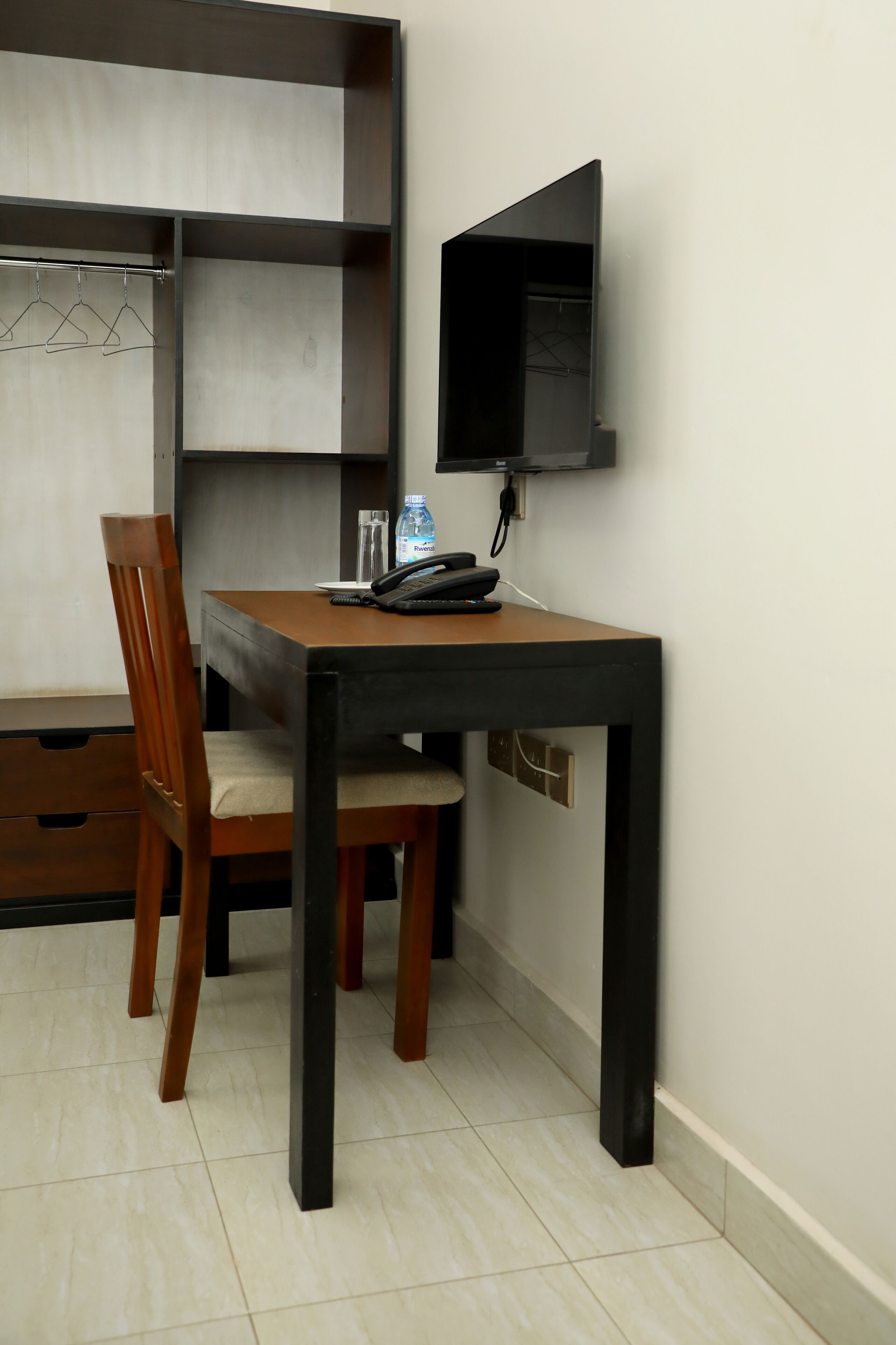 A small, modern room with a wooden table and chairs, a flat-screen TV mounted on the wall, and a water bottle on the table.