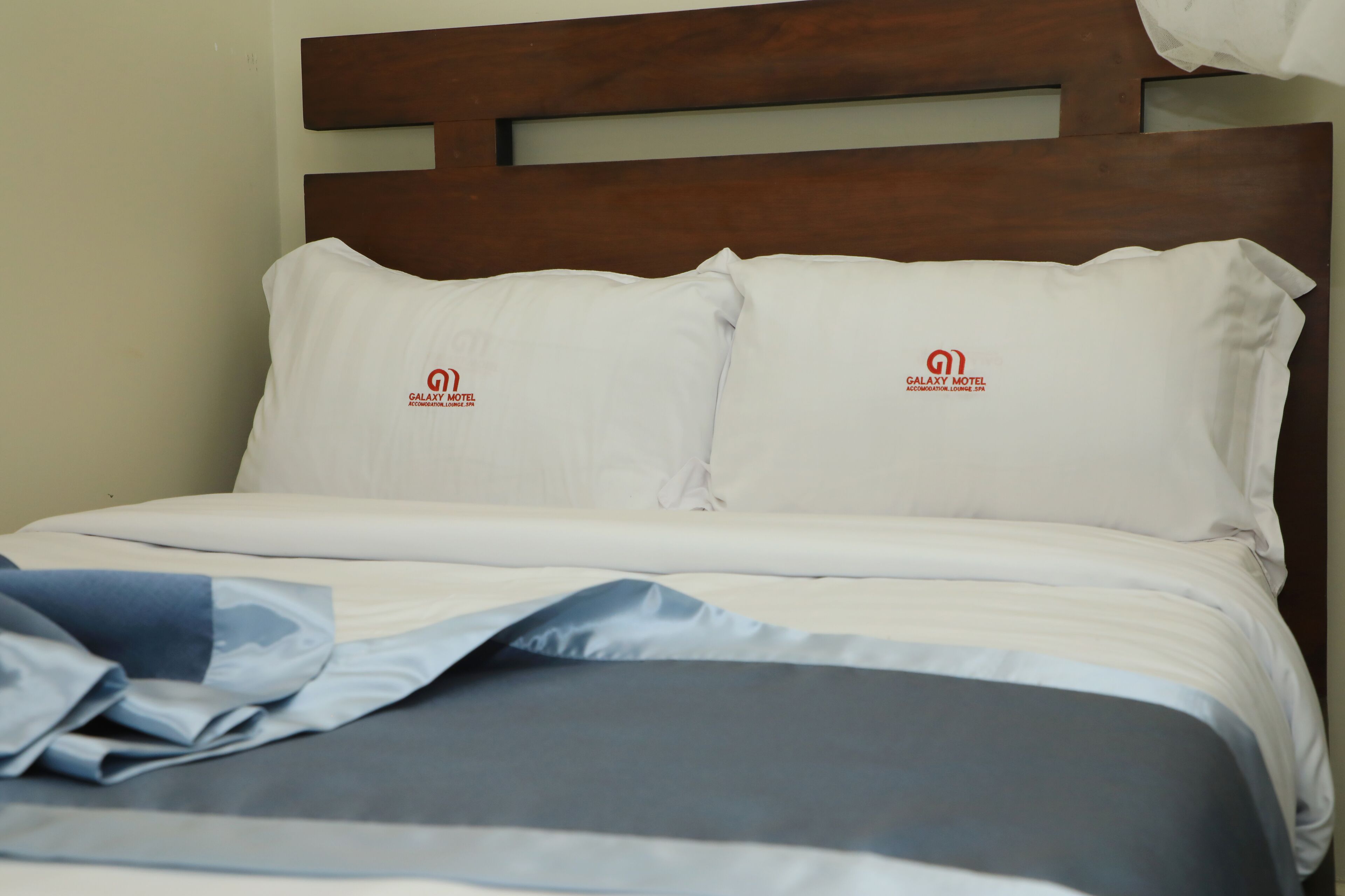 Ein ordentlich bezogenes Bett mit weißer Bettwäsche und zwei Kissen, jeweils mit dem Galaxy Motel Logo.