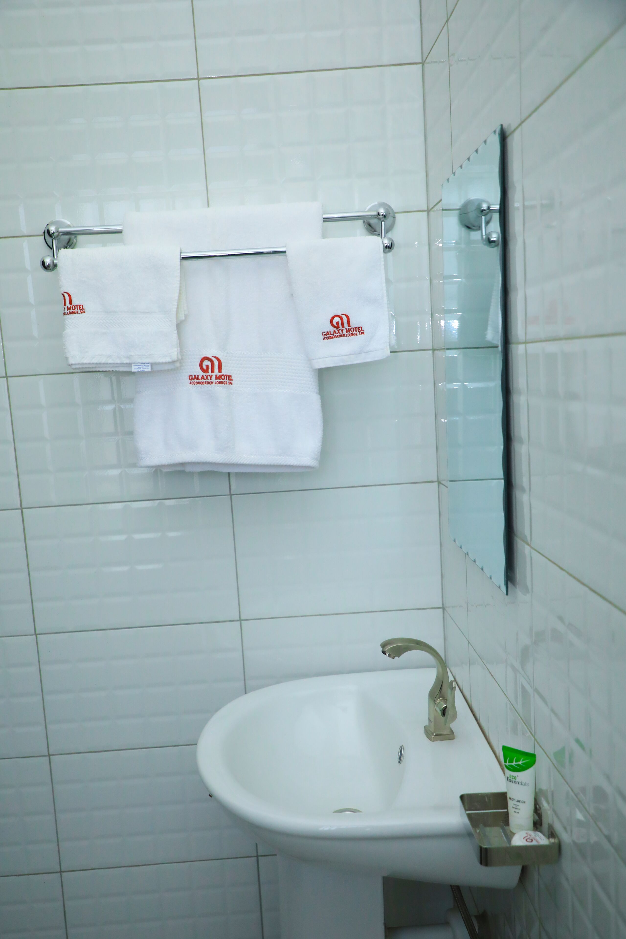 A bathroom with a white sink, a mirror, and two Galaxy Motel towels hanging on a towel rack.