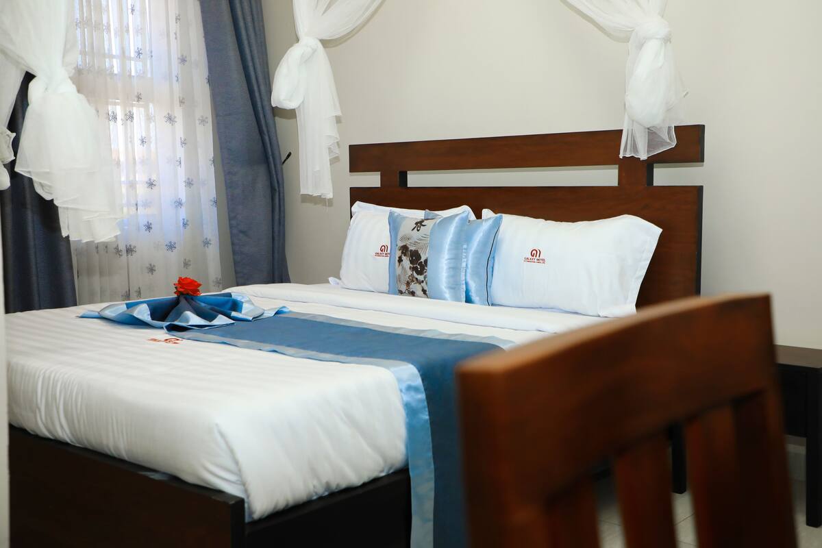 Una cama bien hecha con ropa de cama blanca y azul, cabecera de madera y un arreglo decorativo de almohadas azules y blancas.
