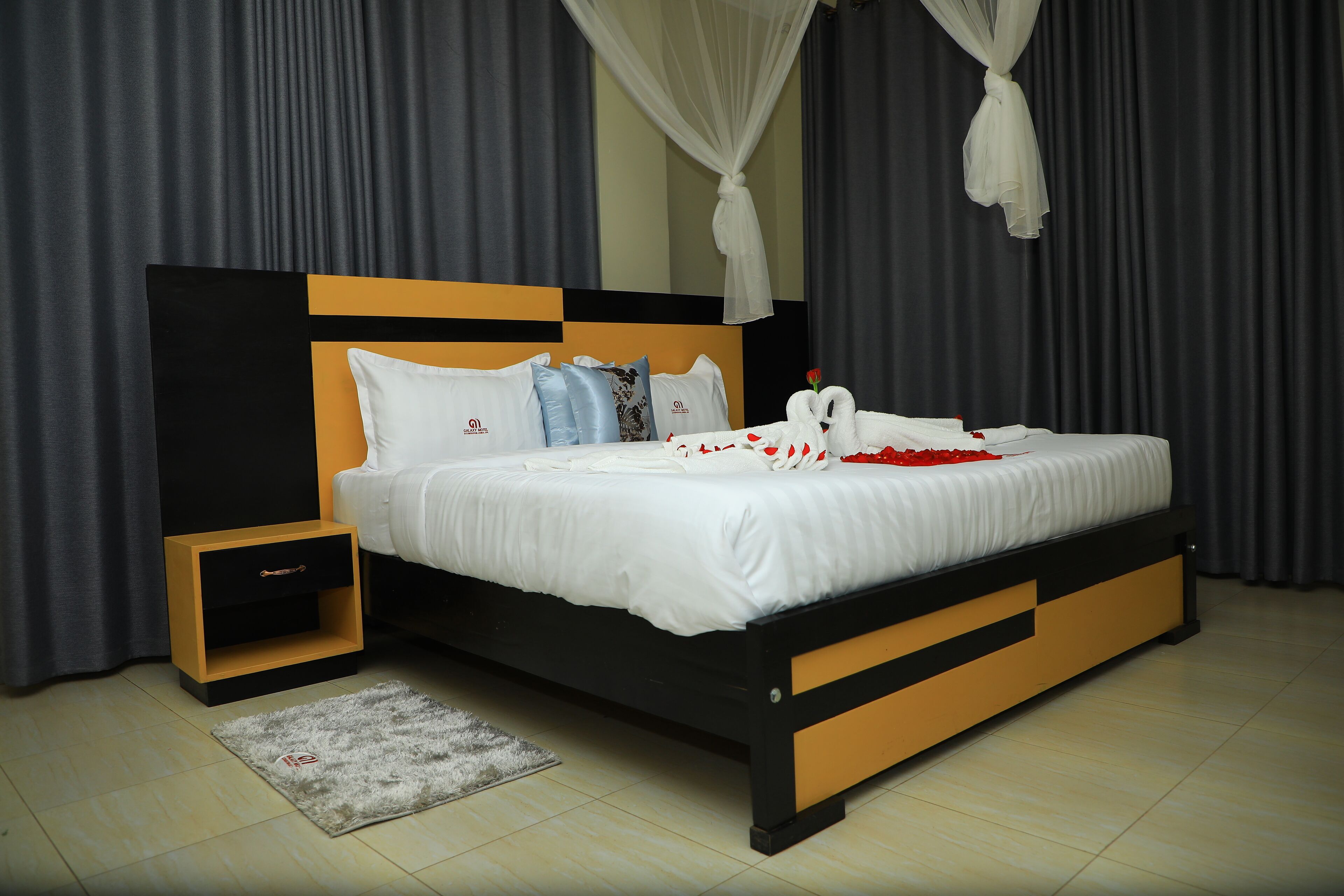 Una cama bien hecha con ropa blanca, una mesita de noche y una alfombra pequeña.