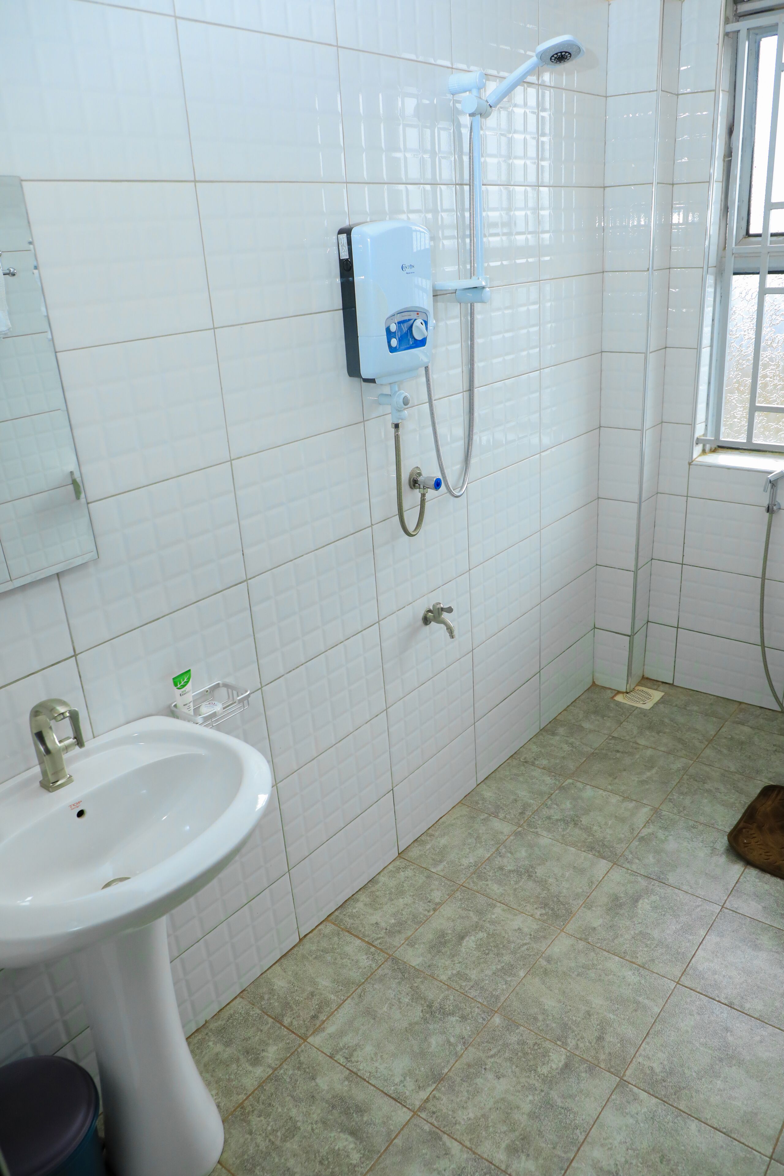 Un baño con lavamanos, espejo, ducha con cabezal de ducha manual y ventana.