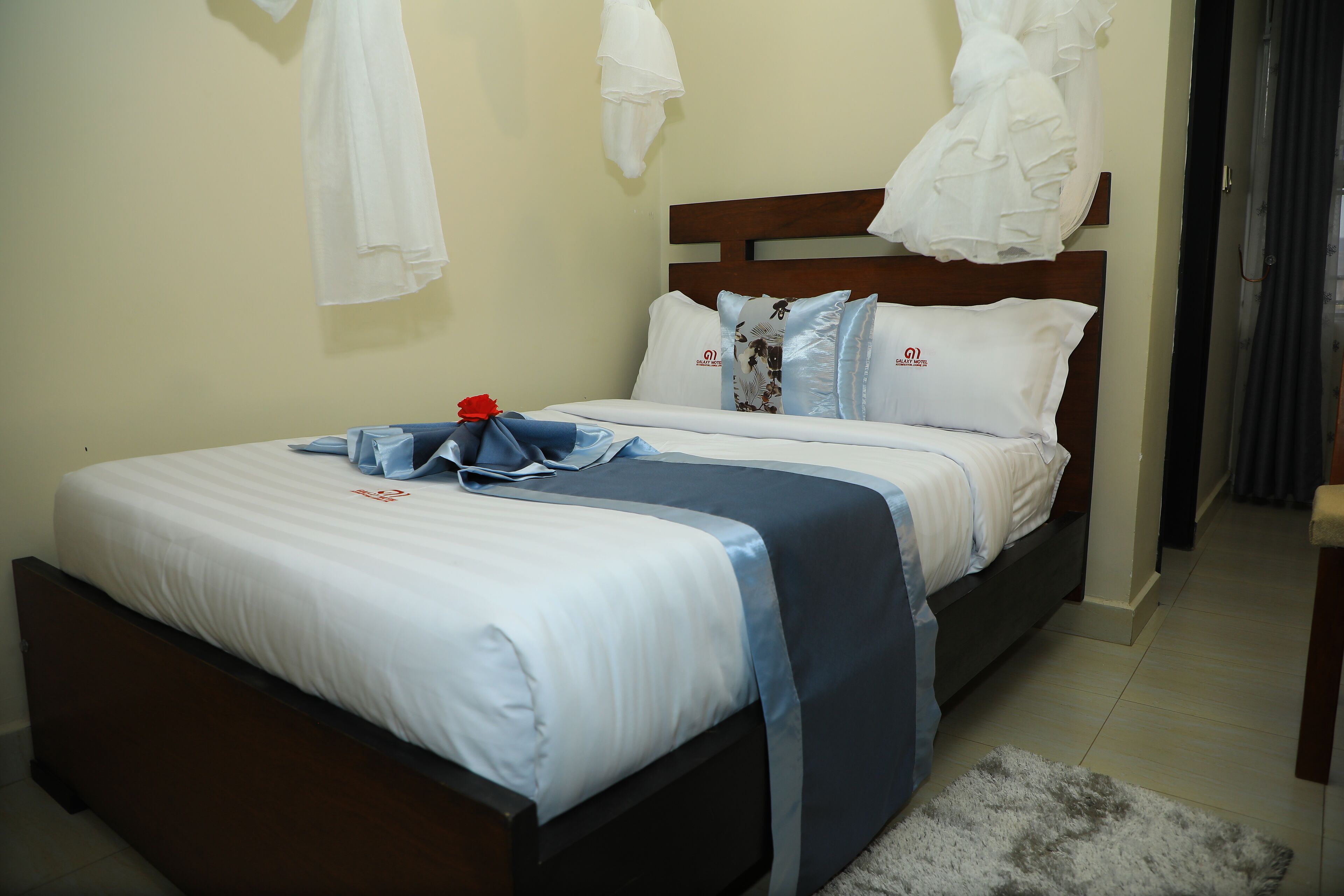 A neatly made bed with white and blue bedding, a wooden headboard, and a small rug on the floor.
