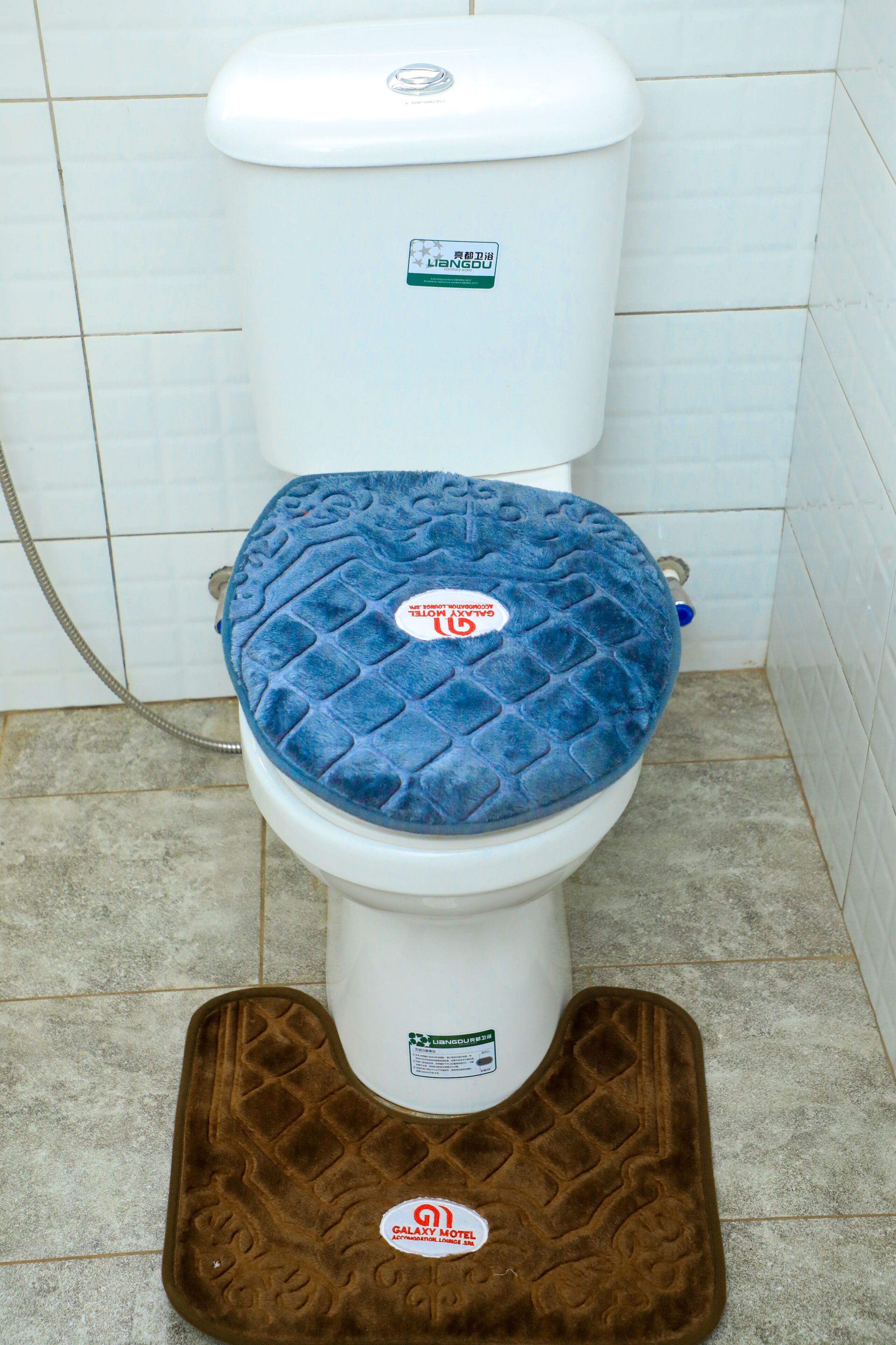 A toilet with a Galaxy Motel branded seat cover and a Galaxy Motel branded mat.