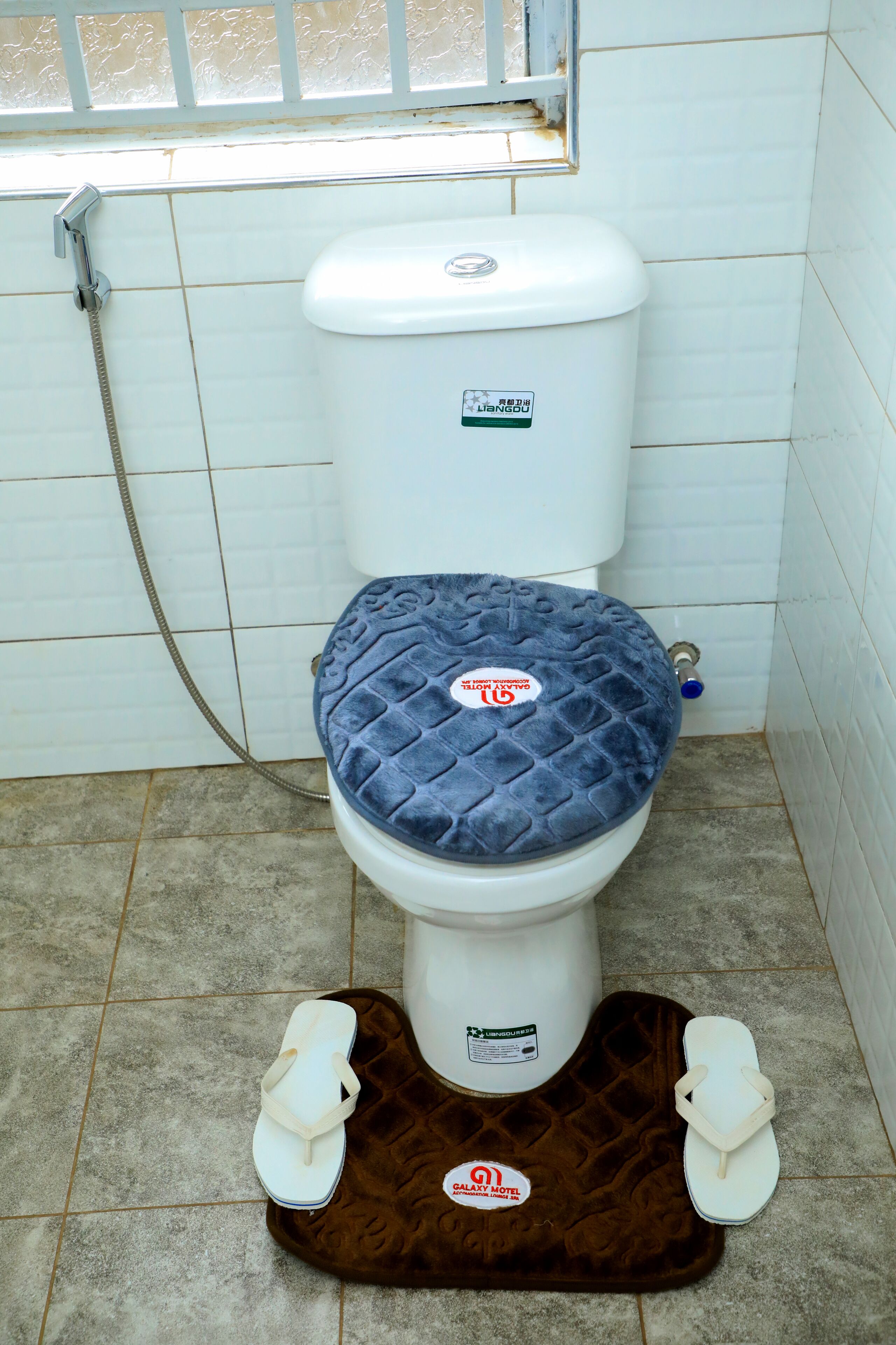 Un inodoro con cubierta acolchada, reposapiés y tubería de agua visible.