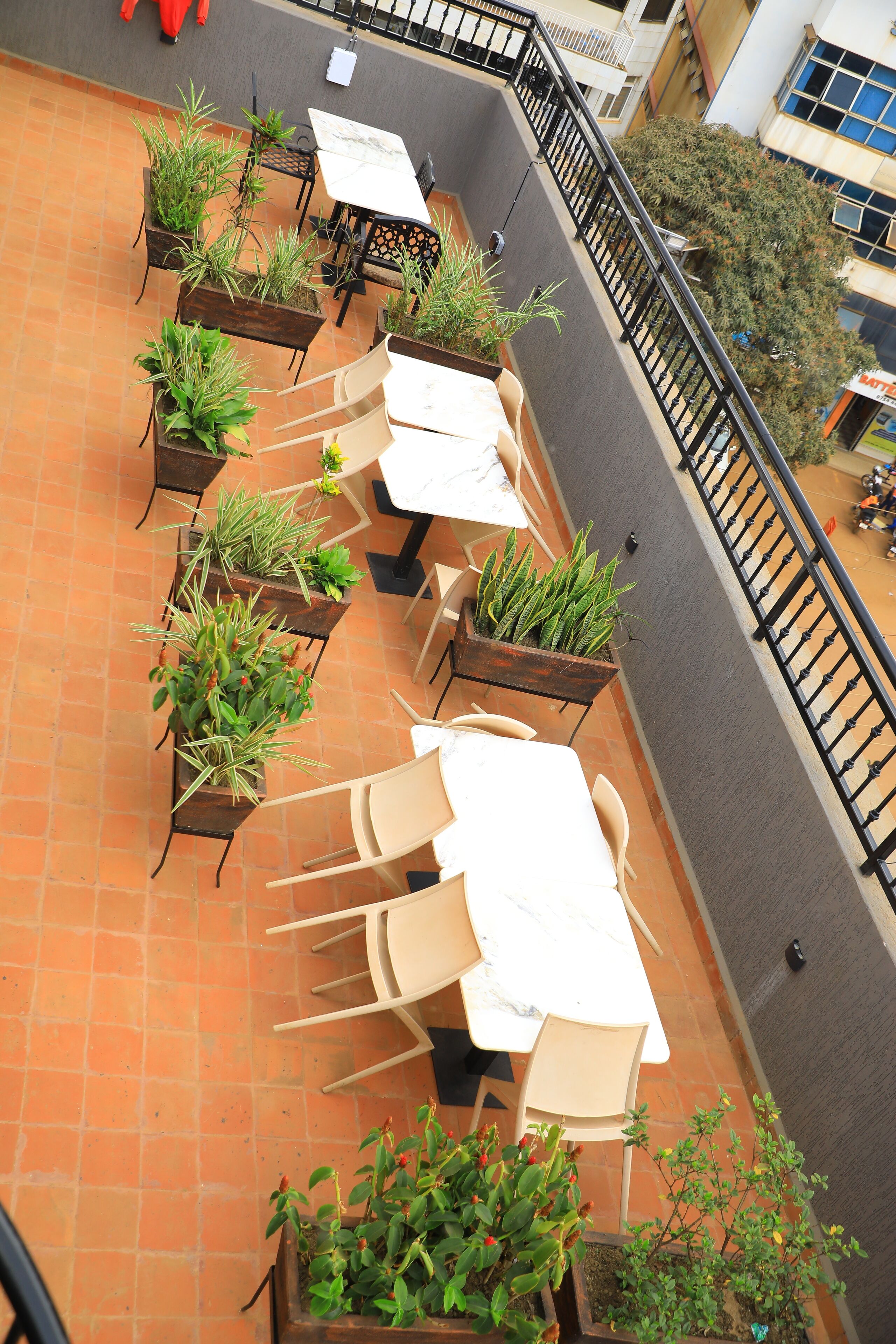 Eine Terrasse im Freien mit mehreren Tischen und Stühlen, umgeben von Topfpflanzen.