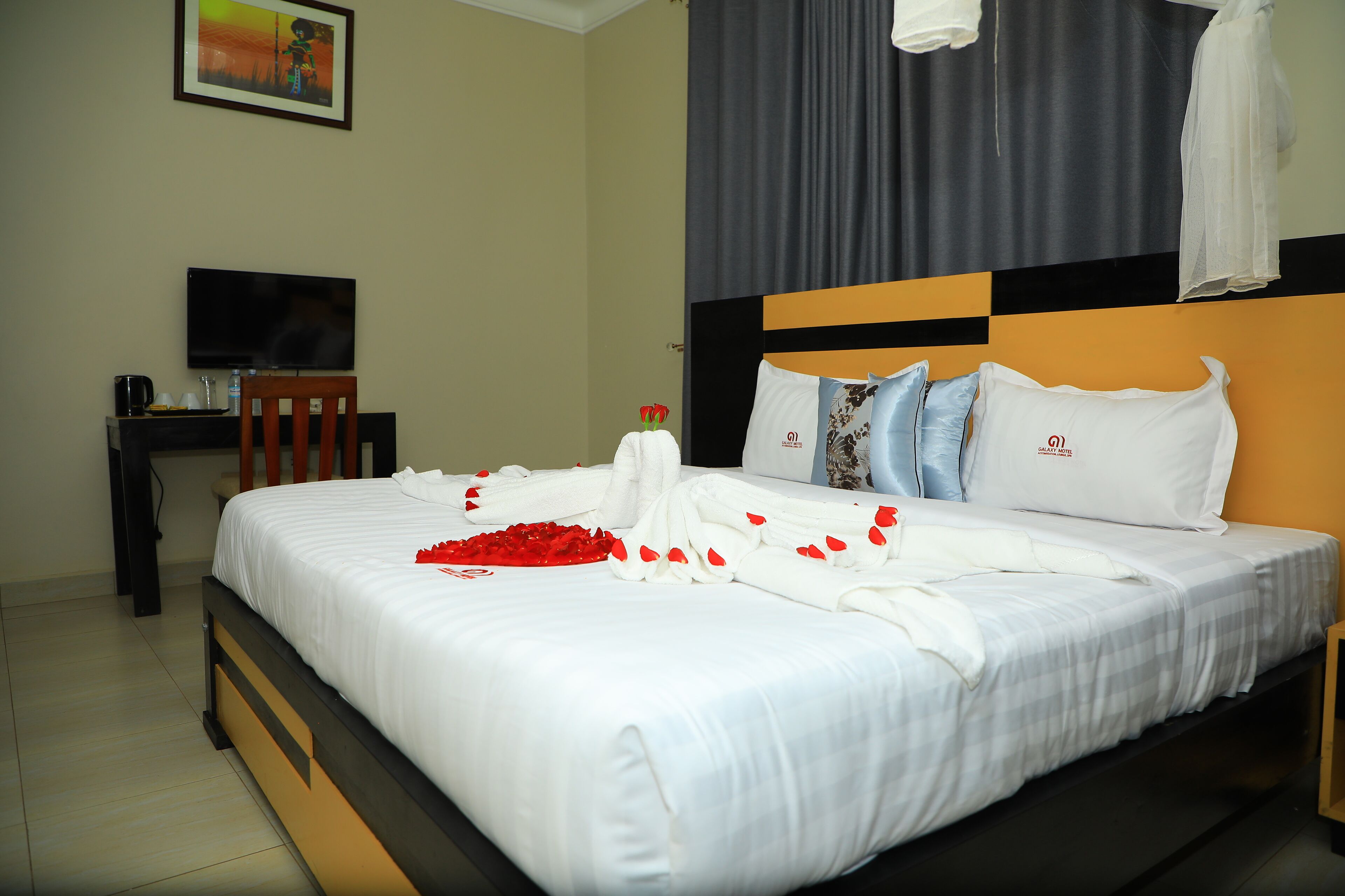 A neatly made bed with white linens, a bouquet of red roses, and a white towel on the side.