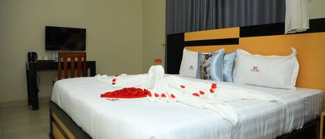 A neatly made bed with white linens, a bouquet of red roses, and a white towel on the side.