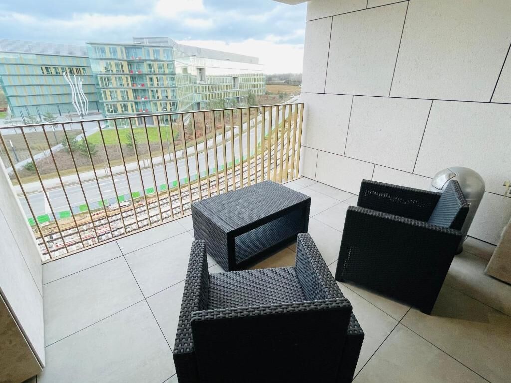 A balcony with a view of modern buildings, a metal railing, and black wicker furniture.