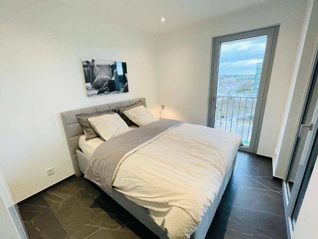 Une chambre à coucher avec un lit, une table de chevet, un tableau au mur et un balcon donnant sur la ville.