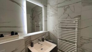 A modern bathroom with a marble backsplash, a large mirror, a sink, and a towel rack. - Luxury Flat with Parking & Large Terrace (Luxembourg City)