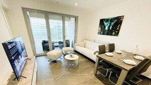 A modern living room with a sofa, a dining table set for four, a TV, and a large window with a view of the city. - Luxury Flat with Parking & Large Terrace (Luxembourg City)