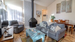 A living room with a sofa, armchairs, a coffee table, a fireplace, and a dining area with wooden chairs and a table.