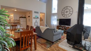 A modern living room with a dining area, a fireplace, and a kitchen in the background.