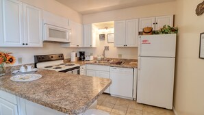 A kitchen with white cabinets, a granite countertop, a microwave, a stove, a sink, and a refrigerator.