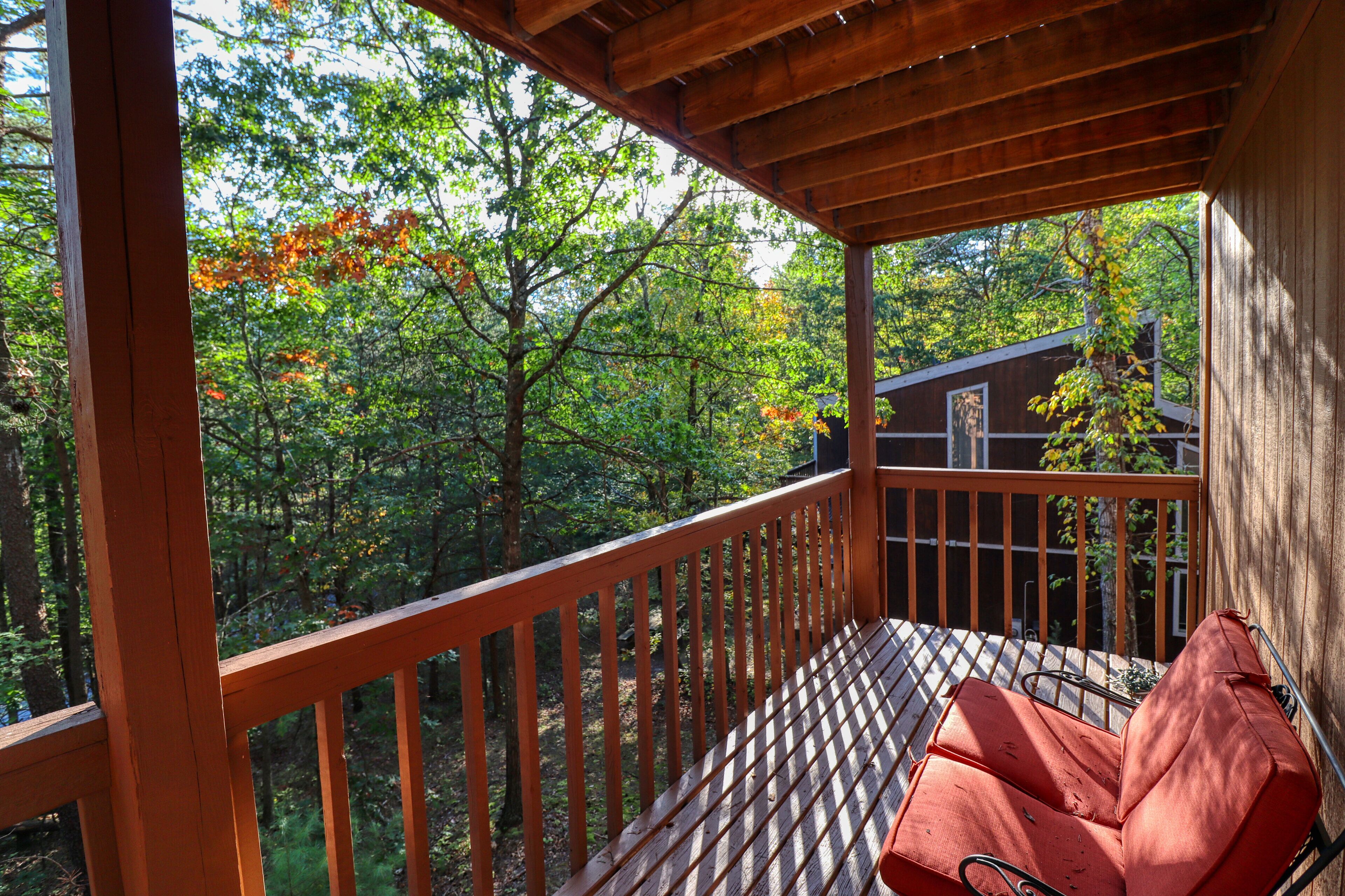 Eine Holzterrasse mit Metallgeländer, einer roten Bank und Blick auf ein von Bäumen umgebenes Haus.