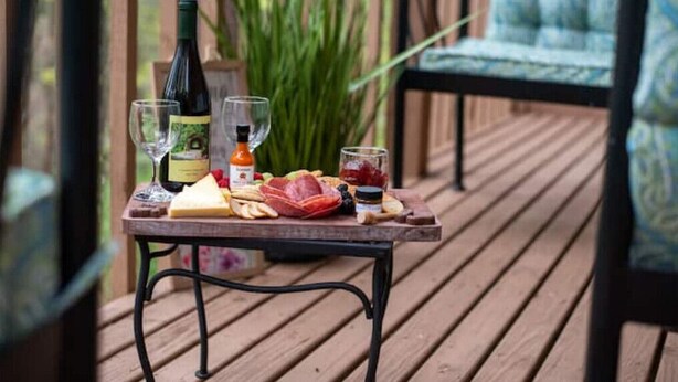 A wooden table with a bottle of wine, glasses, cheese, and meat on a deck.