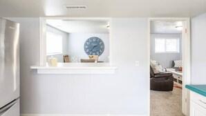 Una cucina moderna con orologio integrato, frigorifero e finestra che si affaccia sulla zona soggiorno.
