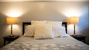 Un letto con lenzuola bianche e due abat-jour, su uno sfondo spoglio.