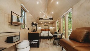 A compact, modern interior with a wooden finish, a kitchenette, a dining area, and a seating area with a brown leather couch.