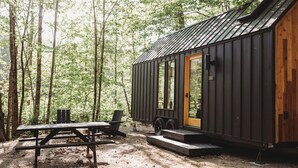 A small cabin with a metal exterior and a wooden door, surrounded by trees.