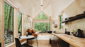A modern cabin interior with a wooden interior, a kitchen with a wooden countertop, a dining area with a table and chairs, and large windows offering a view of the forest.