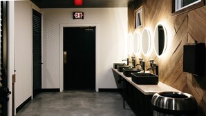 A modern restroom with three sinks, a trash can, and an exit sign.