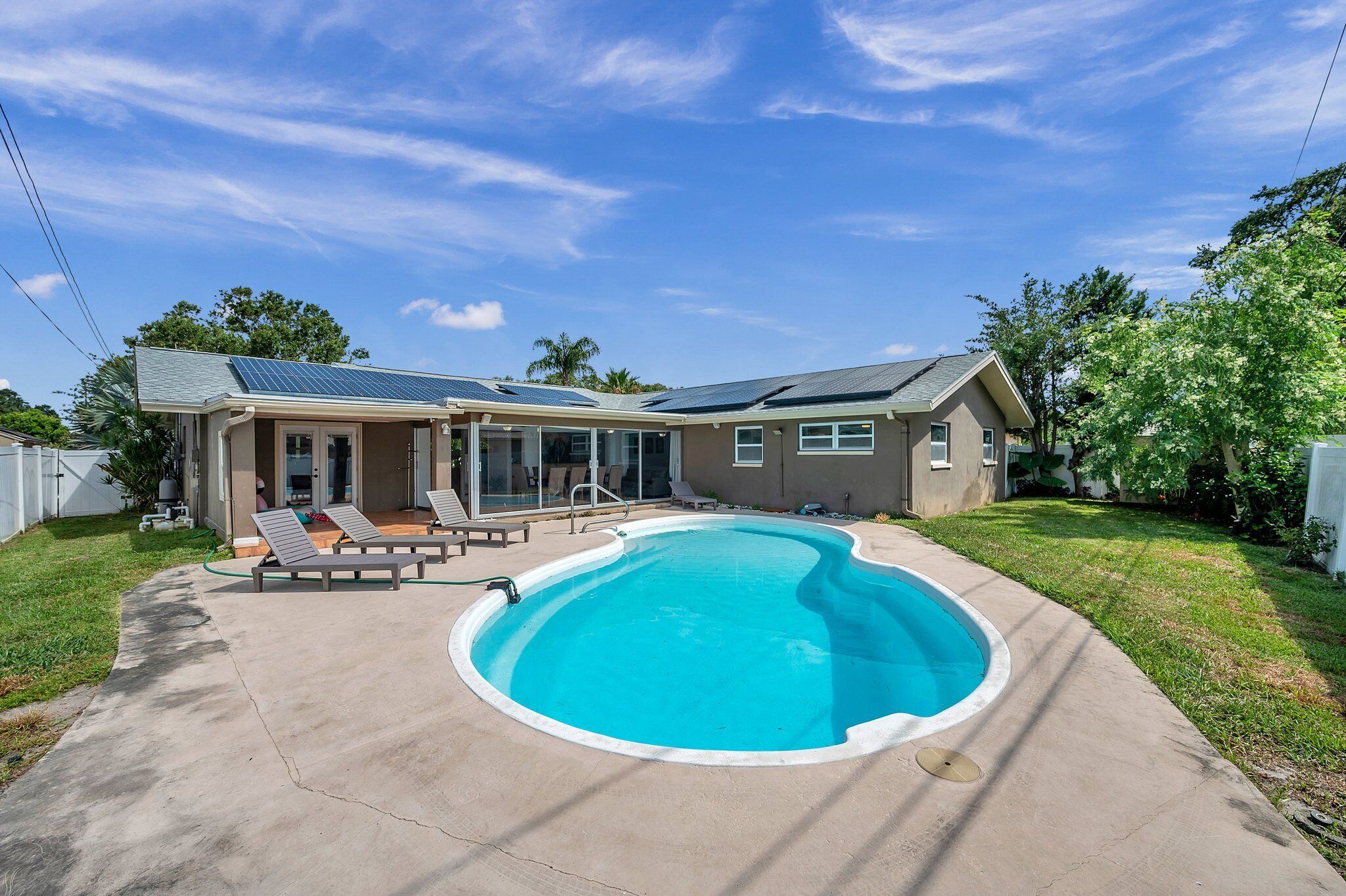 A house with a swimming pool, solar panels, and a covered patio area.