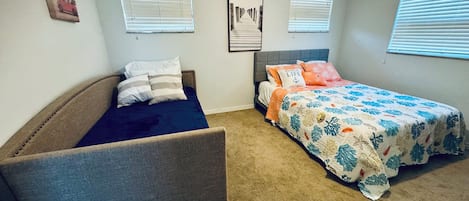 A bedroom with a bed, a couch, and two windows with blinds.