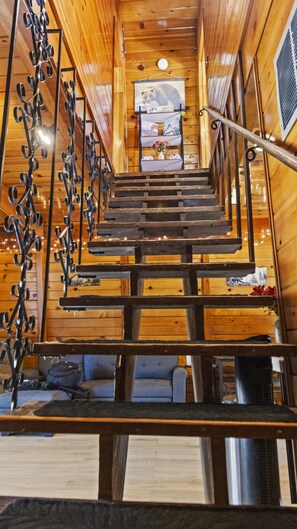 A wooden interior with a central staircase, a hanging light fixture, and a small table with a vase. - Big Bear Cabin Fire Pit, Grill & Trail Access (Big Bear)