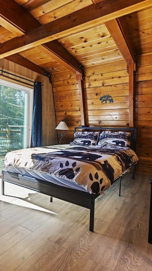 Een slaapkamer in een houten chalet met een bed, een raam met gordijnen en een lamp.