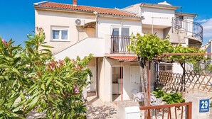 A two-story residential building with a tiled roof, a balcony, and a small garden area with plants and a fence. - Studio Apartment Jagoda (Šibenik-Brodarica)