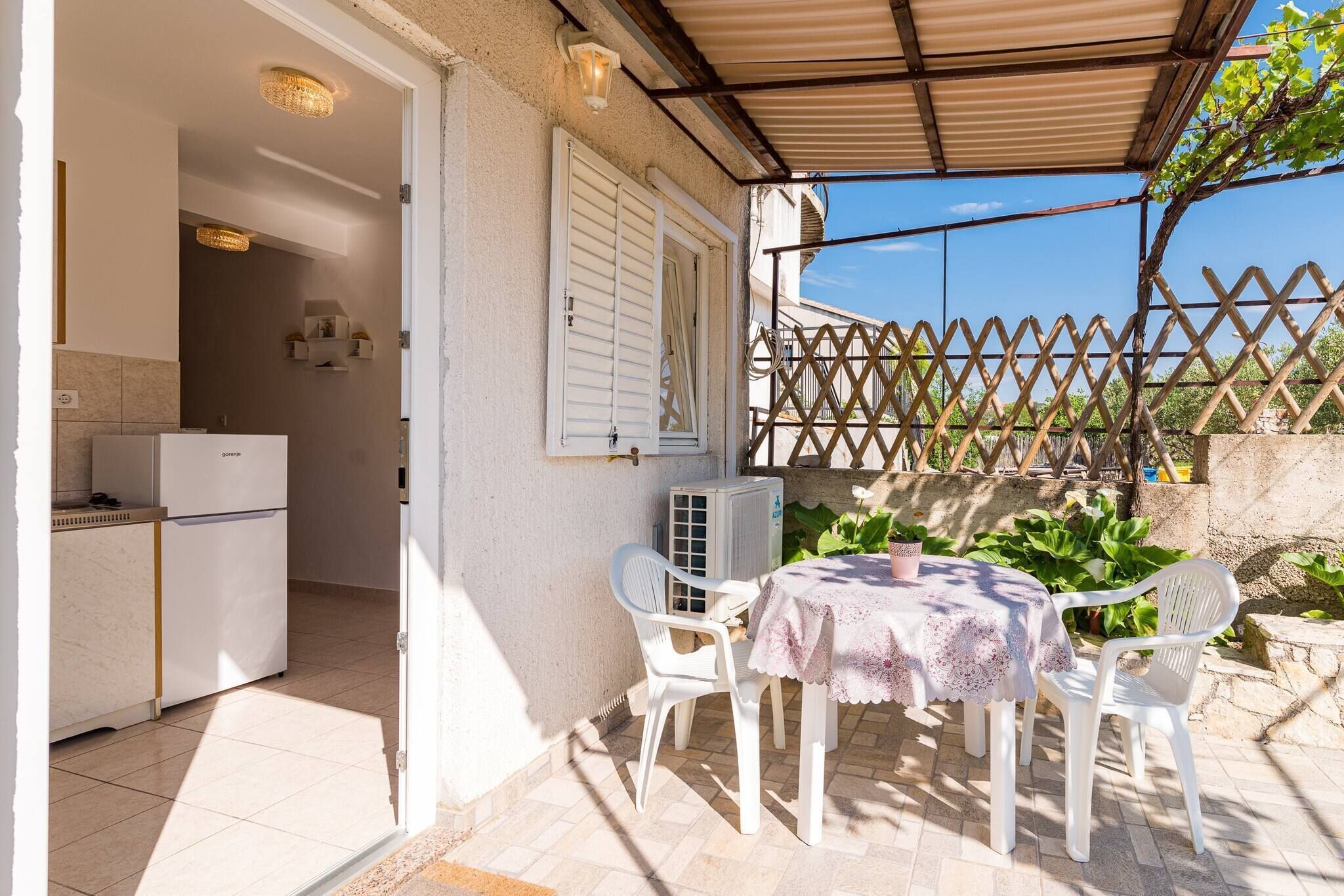 Un patio al aire libre con una mesa, sillas, un refrigerador blanco y una zona cubierta con un cerramiento de celosía.