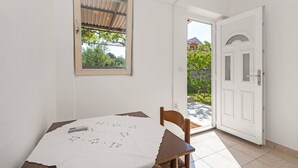 A room with a table, a chair, a window with a view of greenery, and a white door. - Studio Apartment Jagoda (Šibenik-Brodarica)