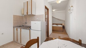 A compact kitchen with a refrigerator, sink, and cabinets. A bed with a wooden headboard is visible in the adjacent room. - Studio Apartment Jagoda (Šibenik-Brodarica)
