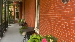 A brick building with a covered porch, outdoor seating, and potted plants. - Historic private guest apartment (Norfolk)