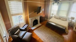 A bedroom with a bed, a fireplace, a TV, and a window with blinds. - Historic private guest apartment (Norfolk)