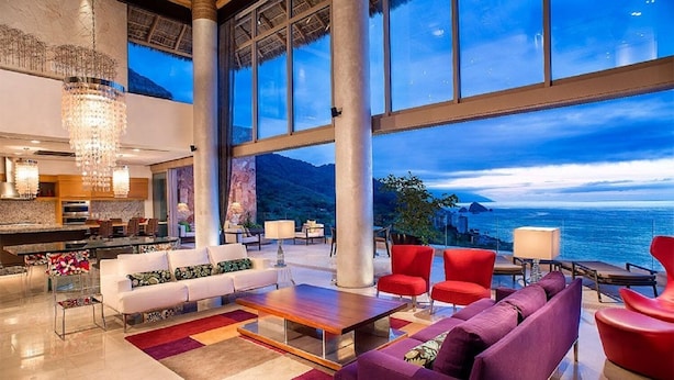 Amplia sala de estar con un ventanal que ofrece vistas panorámicas al océano, una cocina moderna y un candelabro.