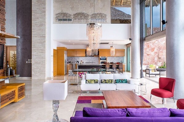 Un amplio salón con una cocina moderna, un comedor y una zona de estar con sofás morados y una silla roja.