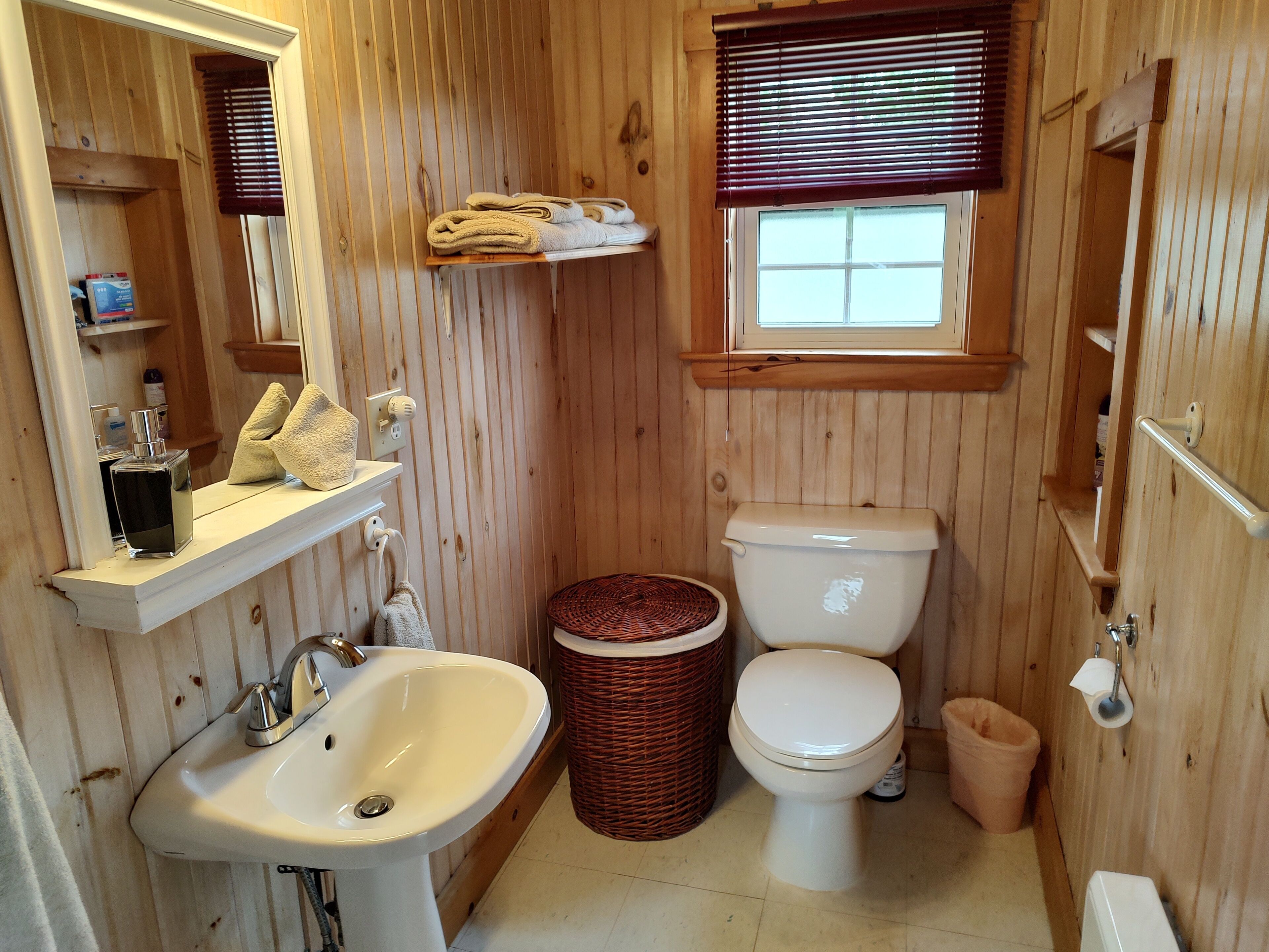 Ein Badezimmer aus Holz mit Waschbecken, Toilette und einem Fenster mit Jalousien.