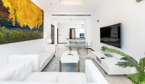 Un salon moderne avec un canapé blanc, une table à manger en verre et un grand tableau accroché au mur.