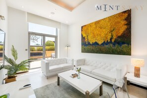 A modern living room with a white sofa, a coffee table, and a large painting of yellow foliage.