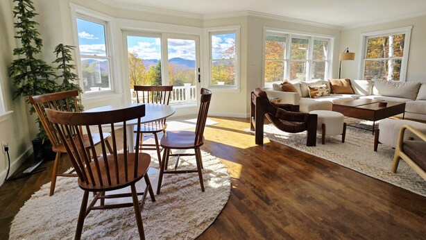 Un salón amplio con comedor, ventanas grandes y vistas a follaje otoñal.